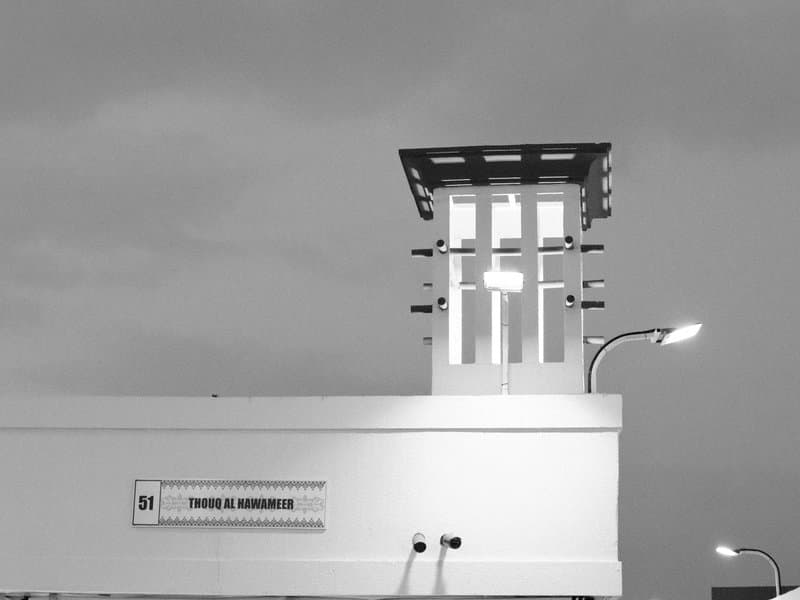 A tall, modern architectural structure with a tower and streetlights against a cloudy sky.