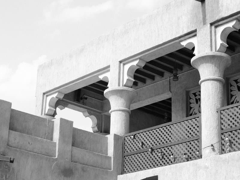 Architectural details of a traditional building with arches and wooden beams against a cloudy sky.