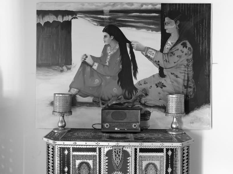 A black and white painting of two women, one styling the other's long hair, displayed above a vintage radio.