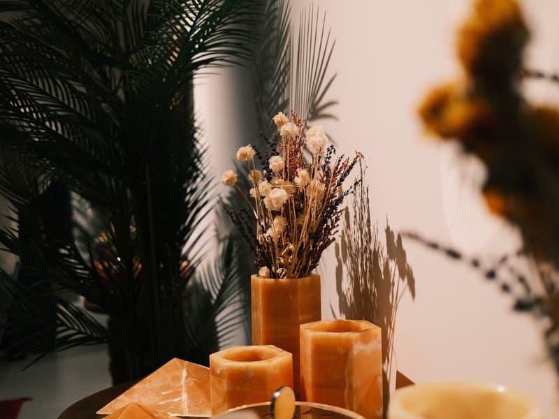 A cozy indoor scene featuring decorative candles and dried flowers against a textured wall.
