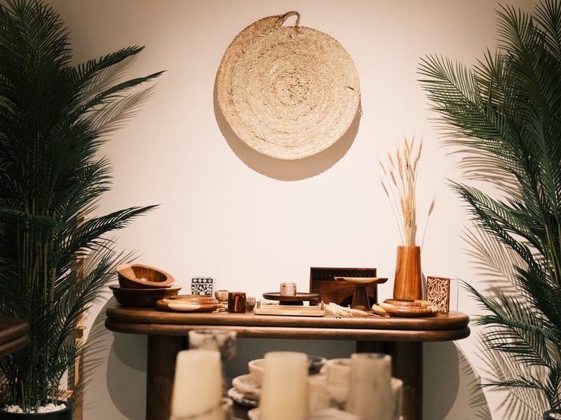 A wooden table adorned with decorative items, surrounded by green plants against a neutral wall.