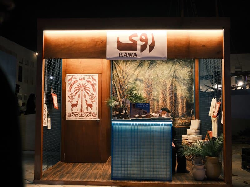 A cozy outdoor stall with a wooden structure, illuminated at night, featuring palm tree artwork.