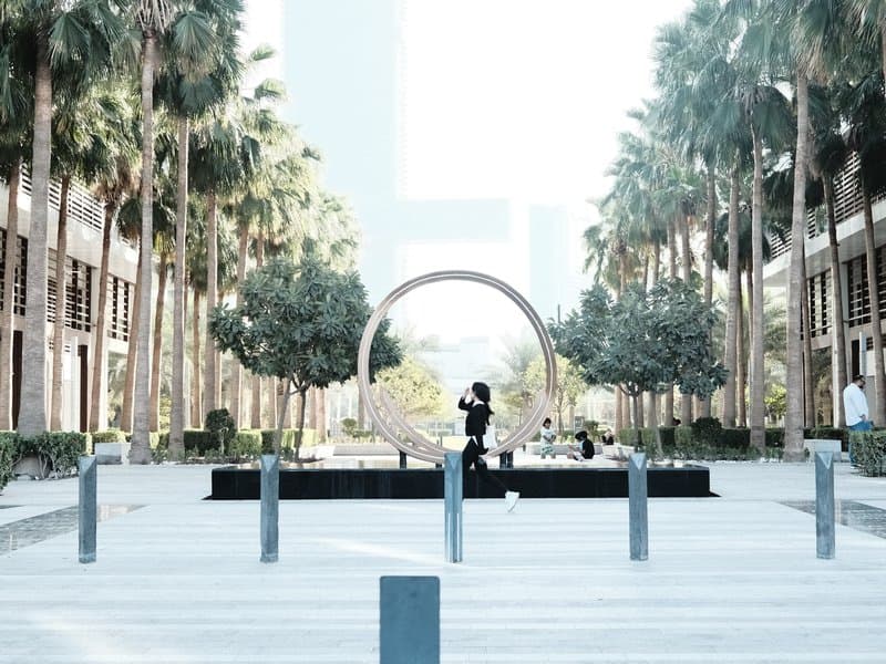 A modern outdoor plaza with palm trees, a circular sculpture, and a couple posing for a photo.