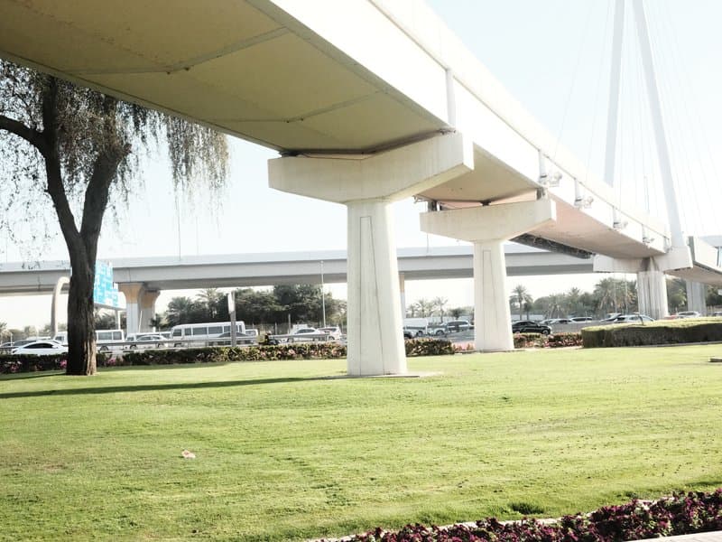 View of a modern bridge supported by concrete pillars, with green grass and vehicles in the background.