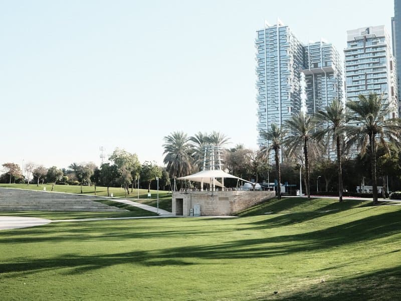 A golf course with a modern building and palm trees, surrounded by tall skyscrapers under a clear sky.