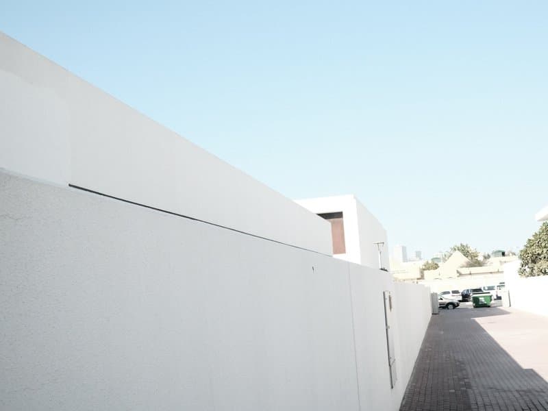 A minimalist architectural scene featuring a white wall against a clear blue sky.