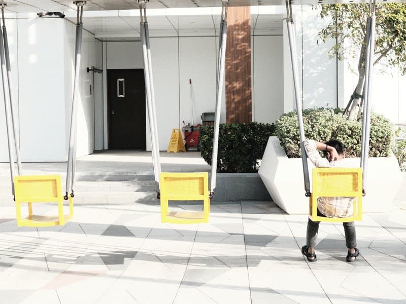 A person sitting on a swing in a modern outdoor space with yellow swings and a minimalist background.