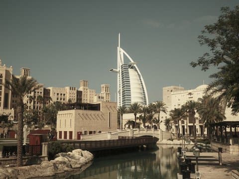 View of the Burj Al Arab with palm trees and buildings along a canal.