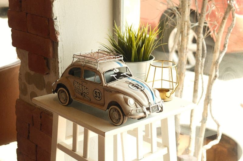 A vintage toy car displayed on a white stool near a potted plant and decorative lantern.