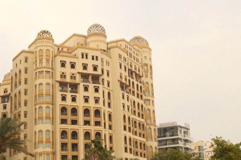 A tall, ornate building with a beige facade and decorative architectural features under a cloudy sky.