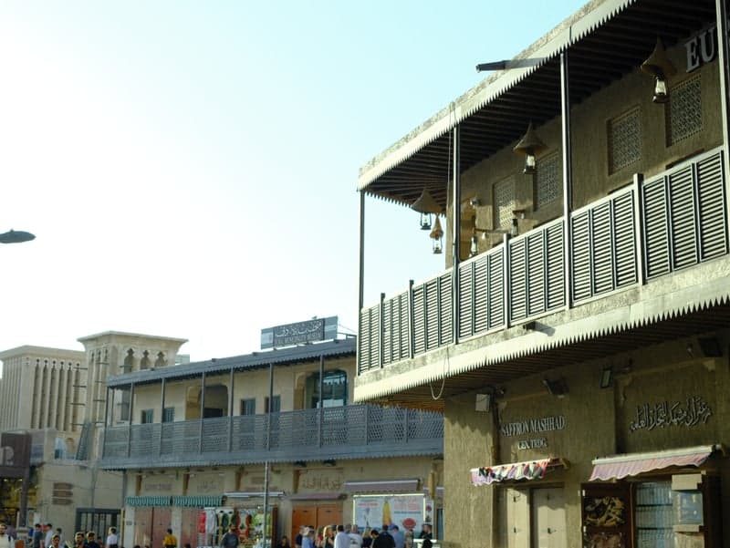 A street scene featuring modern buildings with balconies and shops under a clear blue sky.