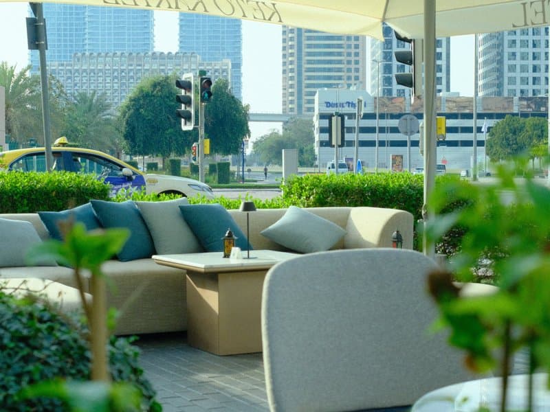 Outdoor seating area with modern furniture and greenery, city skyline in the background.