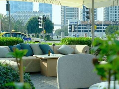 Outdoor seating area with modern furniture and greenery, city skyline in the background.