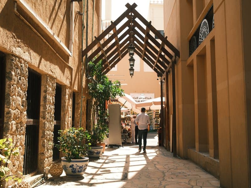 A narrow alleyway with stone walls and wooden beams, featuring a person walking under a canopy.