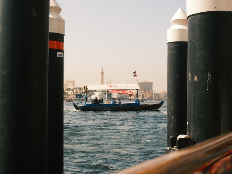 A small boat navigating through water, framed by dock pillars under a clear sky.