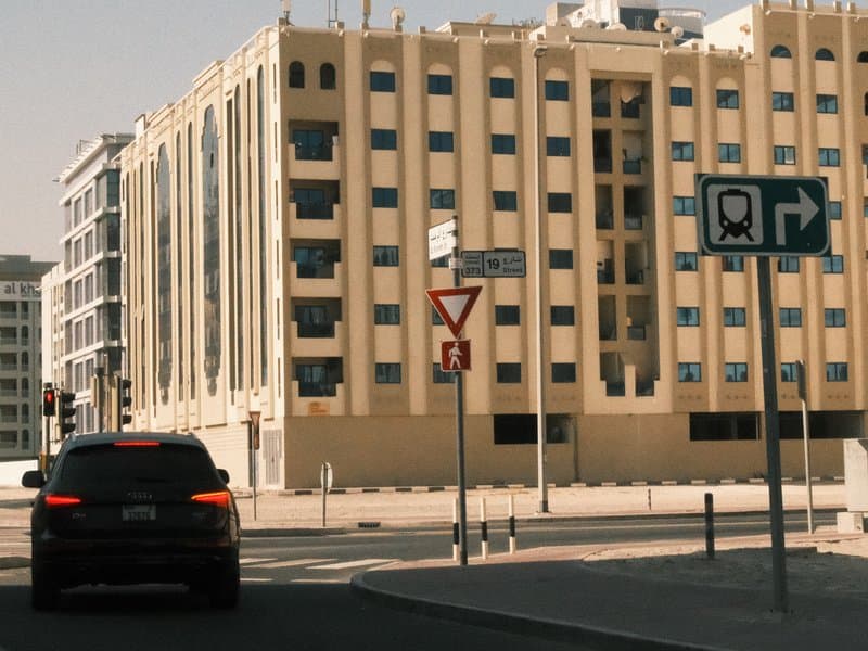 A black car parked near a modern building with a yellow facade and street signs in an urban setting.