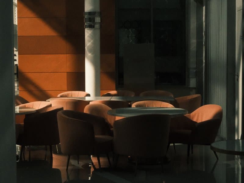 A modern indoor seating area with round tables and plush chairs, illuminated by soft light.