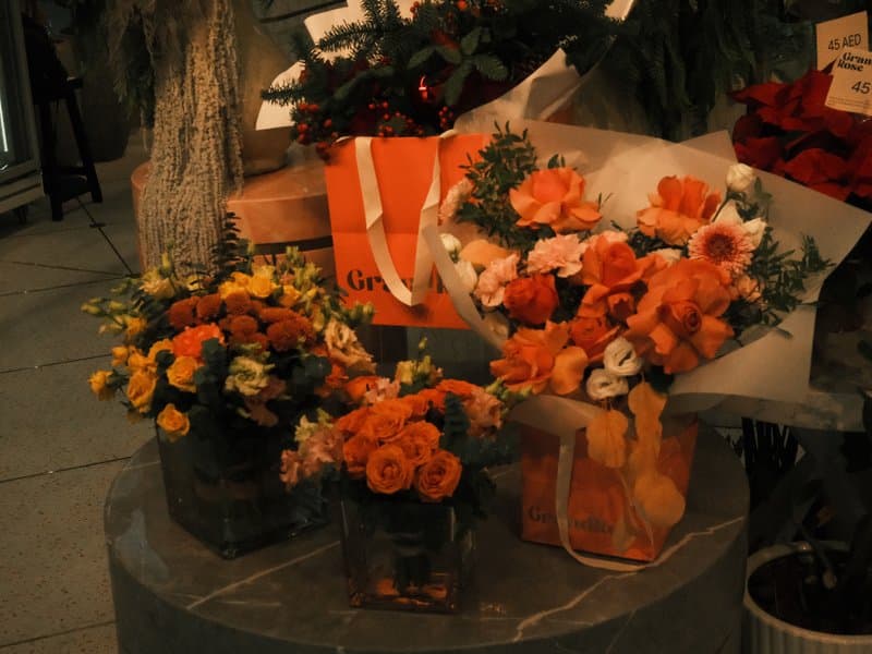 A display of vibrant orange and yellow flower arrangements in various containers on a stone surface.