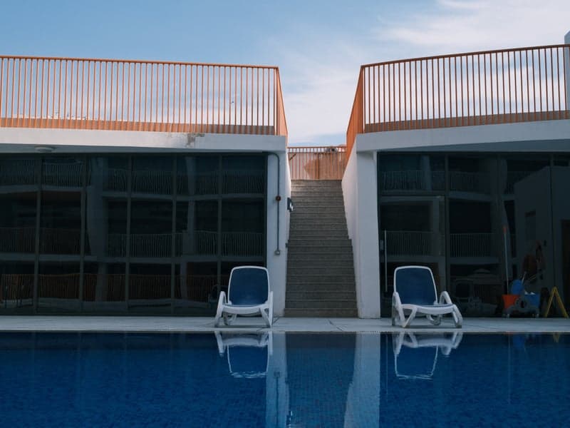 Modern architecture with two buildings facing a swimming pool under a clear blue sky.