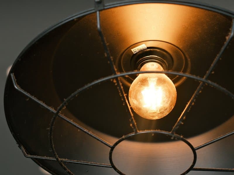 Close-up of a vintage light bulb inside a metal lampshade, glowing warmly.
