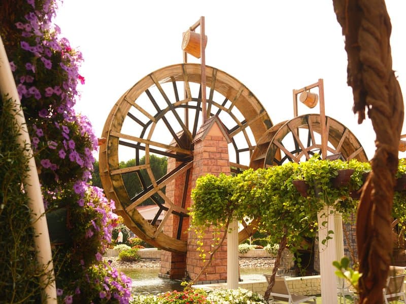Two large wooden water wheels surrounded by vibrant flowers in a garden setting.