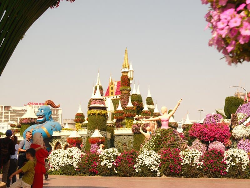 Colorful floral display featuring a castle and characters in a park setting with visitors.