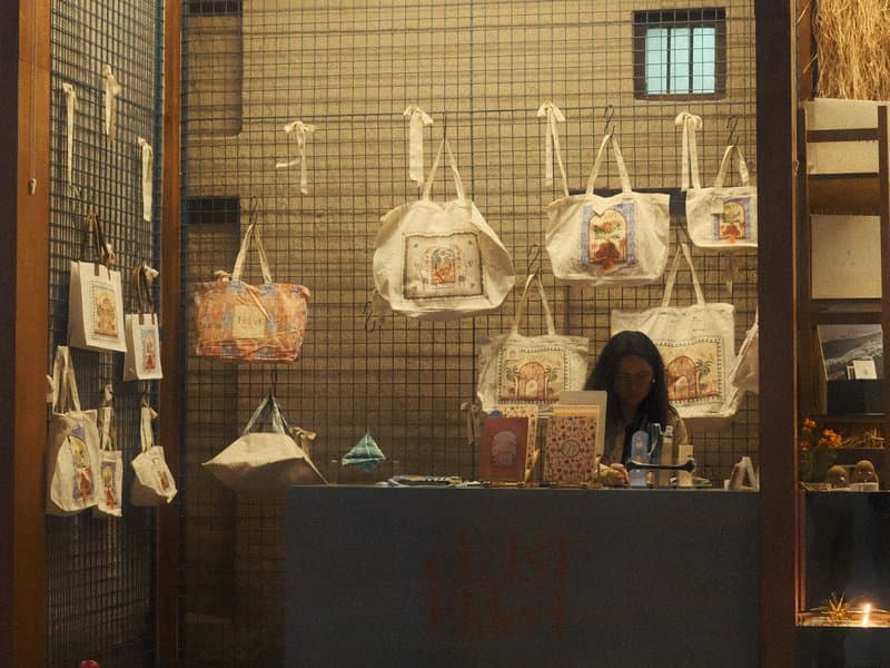 A woman behind a counter in a shop displaying various tote bags and artwork on the walls.