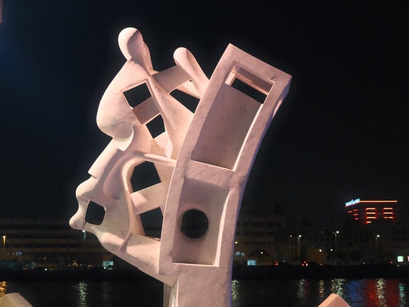 A modern sculpture illuminated at night, showcasing abstract shapes and forms against a dark backdrop.