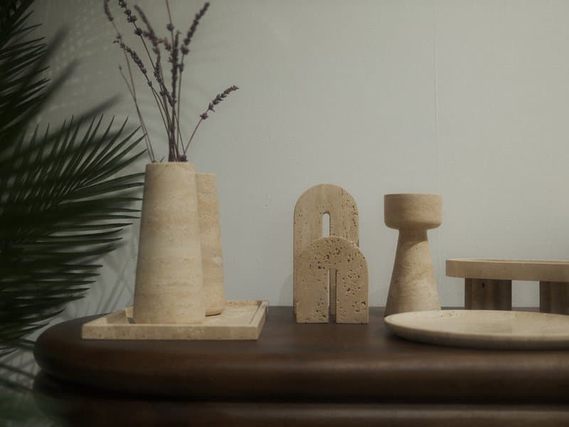 A minimalist still-life arrangement featuring wooden decor items on a table with a plant in the background.
