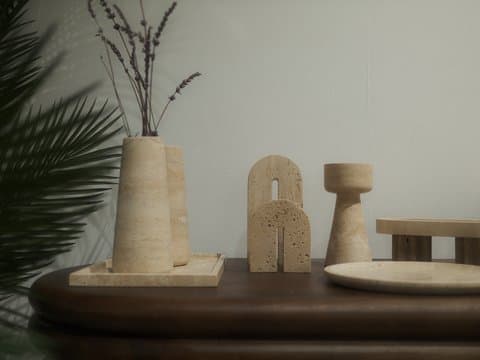A minimalist still-life arrangement featuring wooden decor items on a table with a plant in the background.
