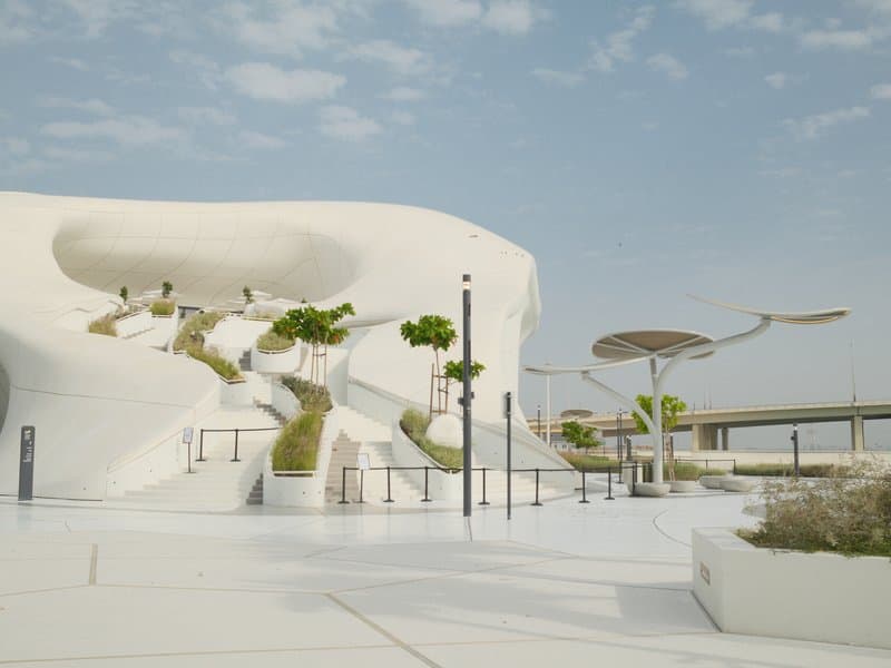 Modern architectural structure with white curves and greenery under a cloudy sky.