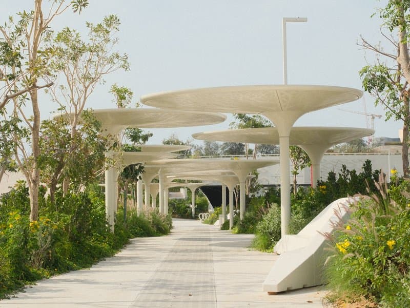A modern pathway lined with unique architectural canopies and greenery on both sides.