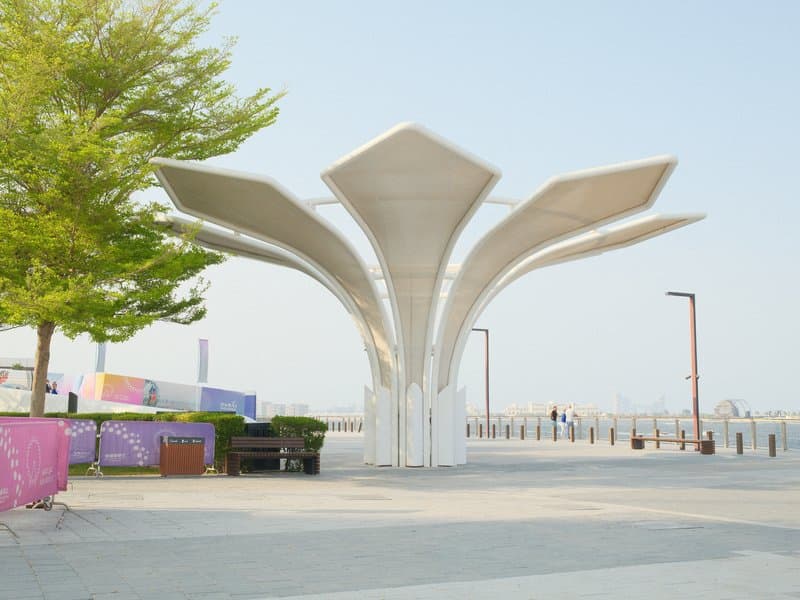 A modern architectural structure resembling a flower, set in an outdoor urban environment with trees.