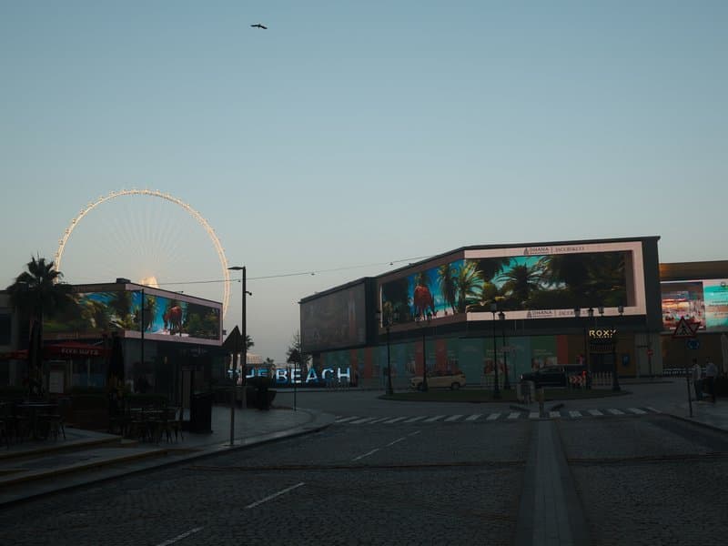 Urban scene featuring large billboards and a Ferris wheel in the background during twilight.