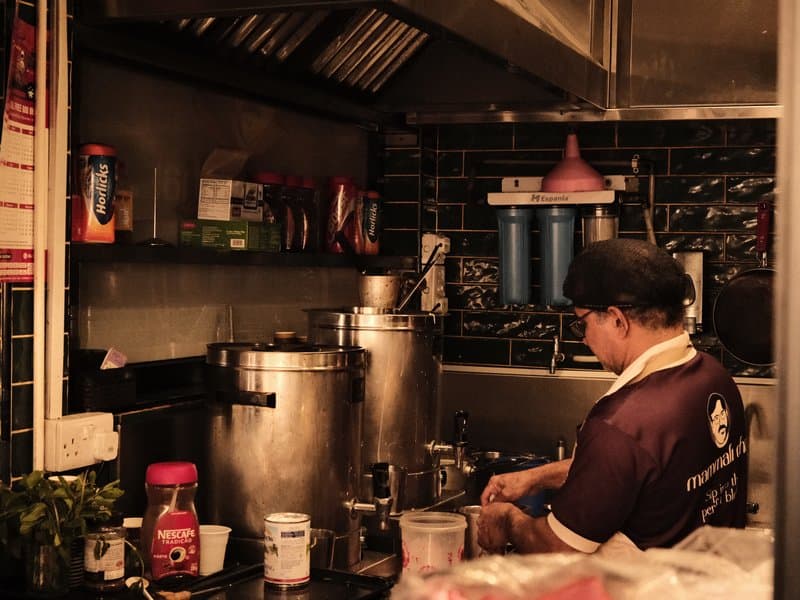 A chef working in a dimly lit kitchen, surrounded by cooking equipment and ingredients.