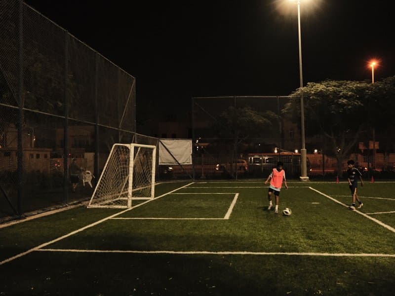 Two players on a soccer field at night, one preparing to kick a ball near the goal.