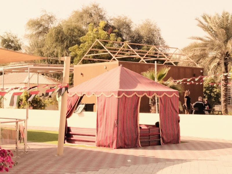 A pink tent in a garden setting with palm trees and a building in the background.