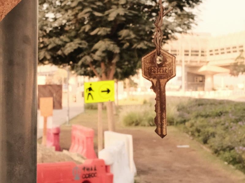 A close-up of a key hanging in the foreground with a blurred urban construction site in the background.