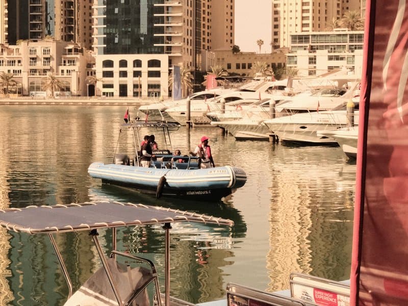 Two people in a small boat on a calm marina with tall buildings in the background.