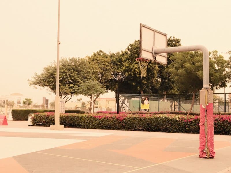 A basketball hoop in a park with a hazy sky and trees in the background.