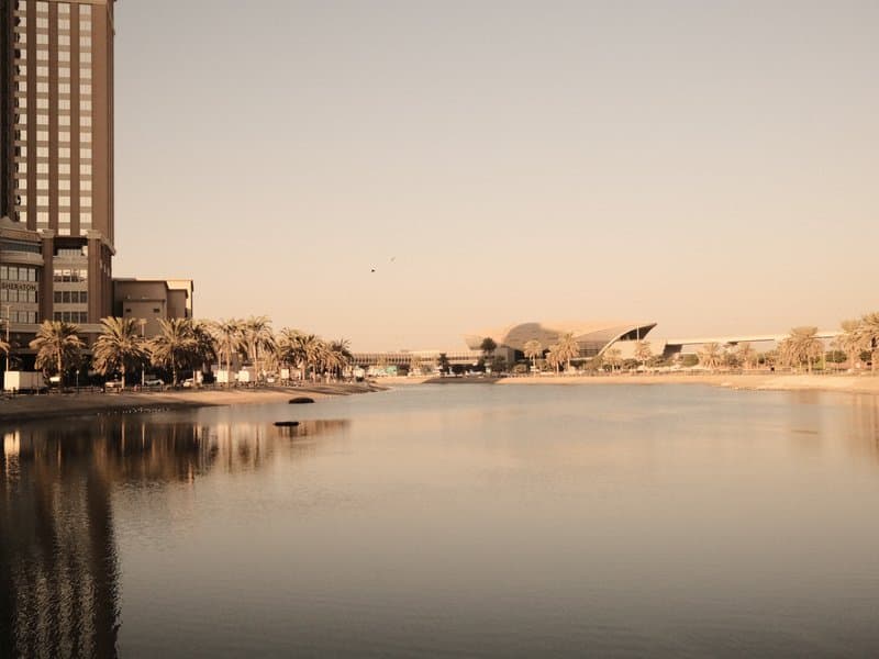A serene river scene with reflections of buildings and trees under a soft, warm light.