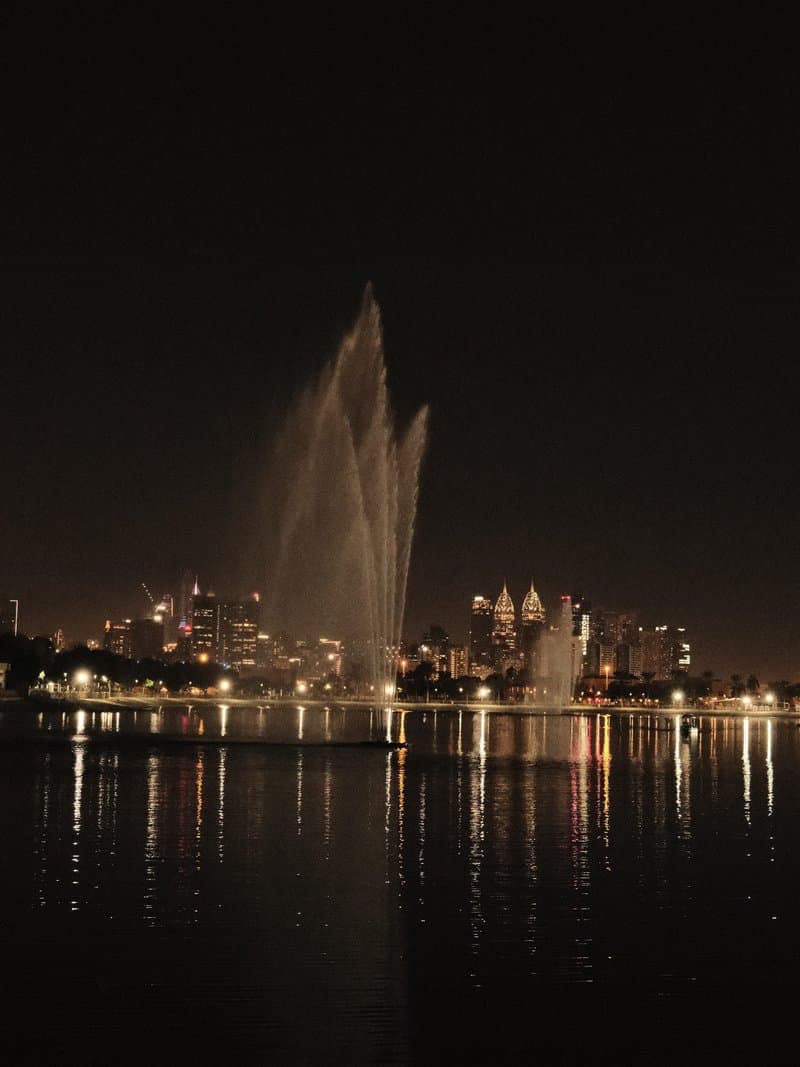 Night view of a fountain with city skyline reflections in the water.