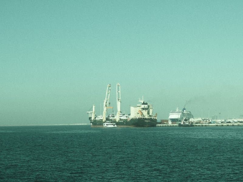 A view of large ships docked at a port with calm waters and a clear sky.