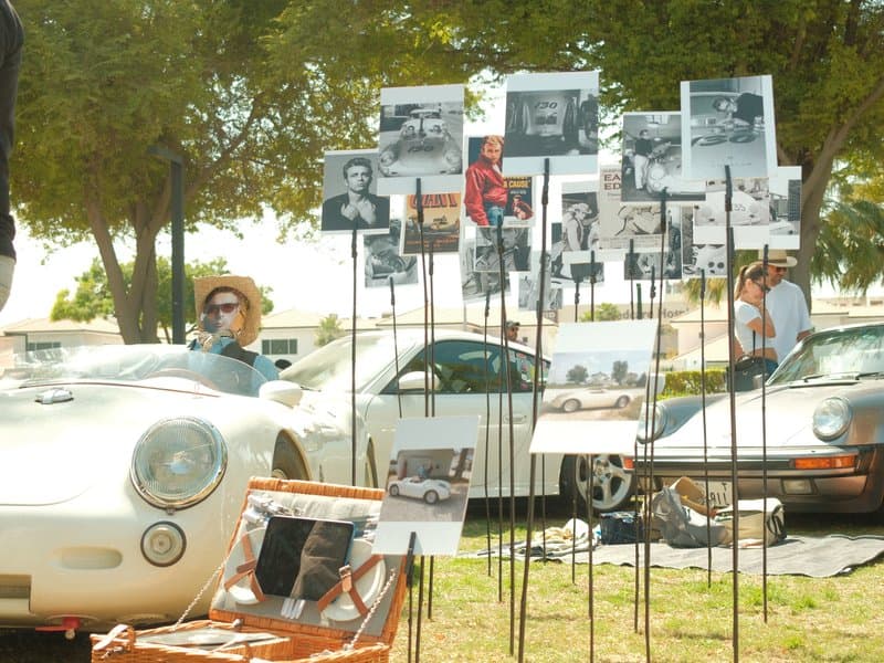 A vintage car show with photographs displayed on stands, showcasing classic cars and attendees enjoying the event.