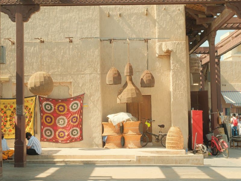 A rustic outdoor market scene featuring traditional baskets, colorful fabric, and a person sitting nearby.