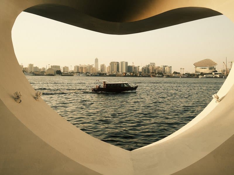 A boat sailing on water framed by a heart-shaped structure with a city skyline in the background.