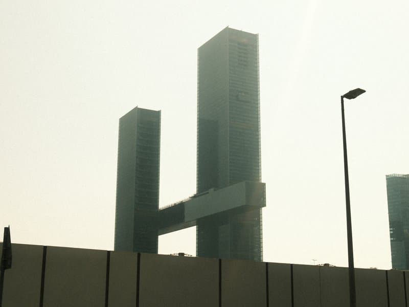 Two tall modern buildings connected by a horizontal structure, shrouded in a hazy atmosphere.