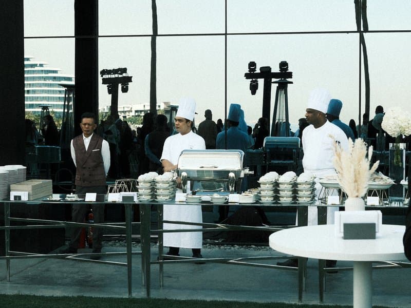 Three chefs preparing food at a modern outdoor event with a city skyline in the background.