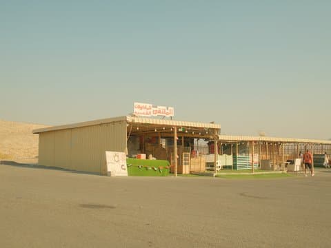 A small roadside shop with colorful wooden stalls under a clear sky, surrounded by sandy terrain.