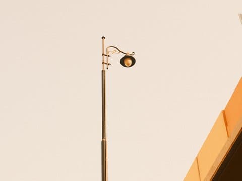 A tall street lamp against a pale sky, with a portion of a building visible in the foreground.